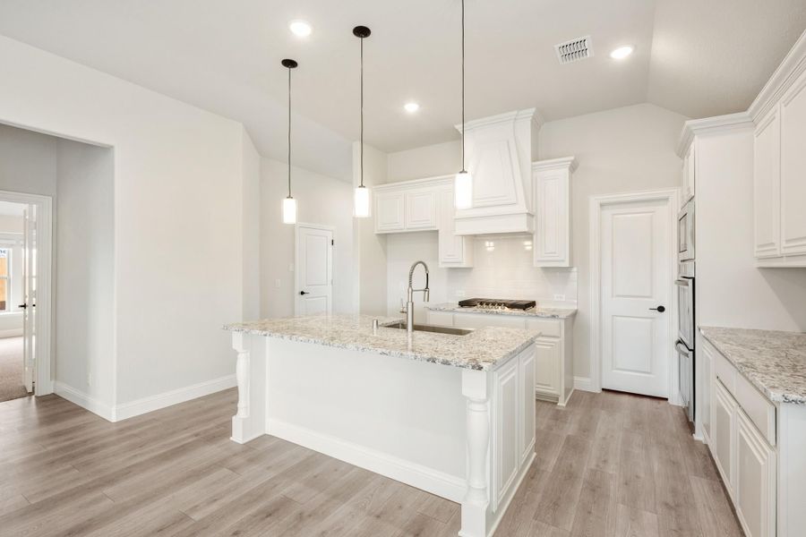 White kitchen with large island, granite countertops, pendant lights, and light wood floors White kitchen with large island, granite countertops, pendant lights, and light wood floors