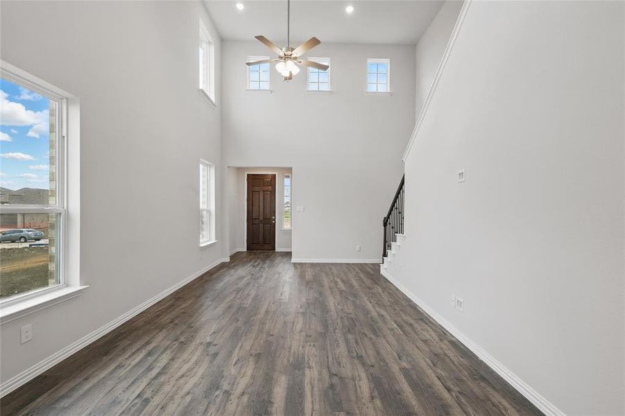 Unfurnished living room featuring dark wood-type flooring, a ceiling fan, stairway, a high ceiling, and recessed lighting