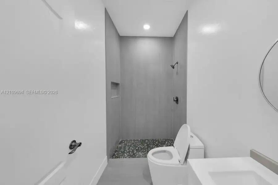 Full-height tiled shower surround with an integrated recessed wall niche, pebble-stone shower floor, matte black shower hardware, and a high-efficiency toilet