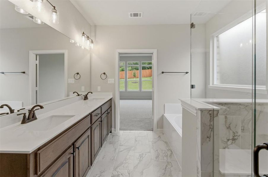 Bathroom featuring a dual vanity with dark wood cabinetry and white countertops, a large mirror with overhead lighting, a built-in bathtub, and a glass-enclosed shower with marble-look tile accents