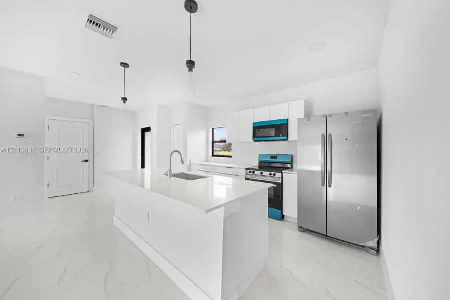 Kitchen featuring a central island with a quartz countertop, white flat-panel cabinetry, stainless steel appliances, and large-format tile flooring Kitchen featuring a central island with a quartz countertop, white flat-panel cabinetry, stainless steel appliances, and large-format tile flooring