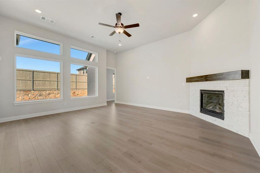 Unfurnished living room featuring a stone fireplace, a ceiling fan, a high ceiling, recessed lighting, and light wood-style flooring