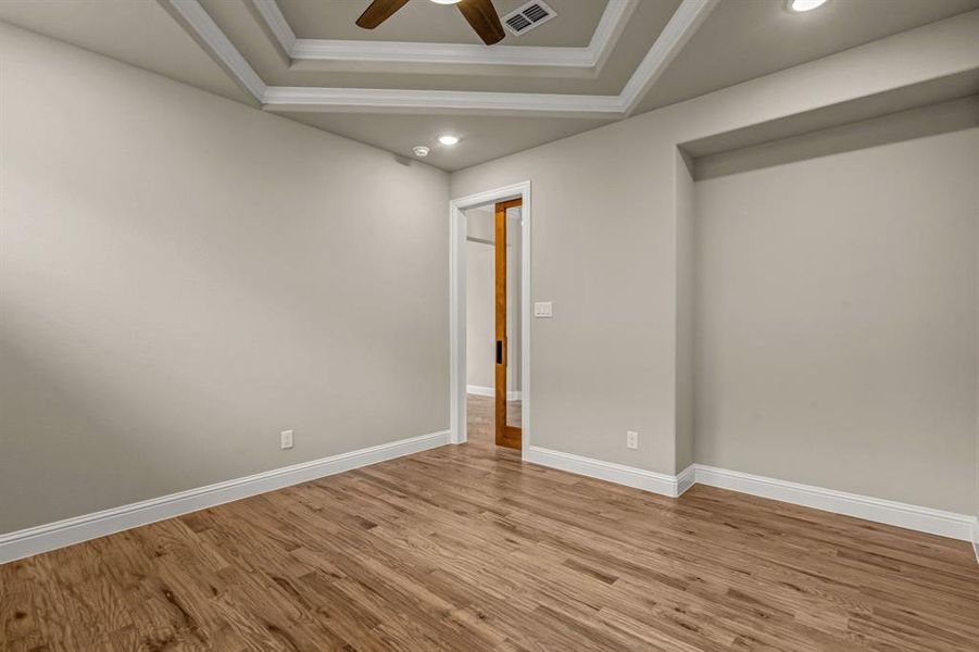 Empty room with a tray ceiling, ceiling fan, wood finished floors, crown molding, and recessed lighting