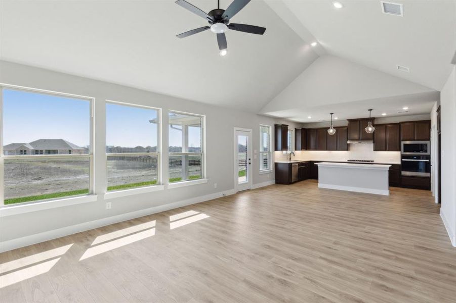 Unfurnished living room featuring visible vents, baseboards, light wood-type flooring, high vaulted ceiling, and a sink