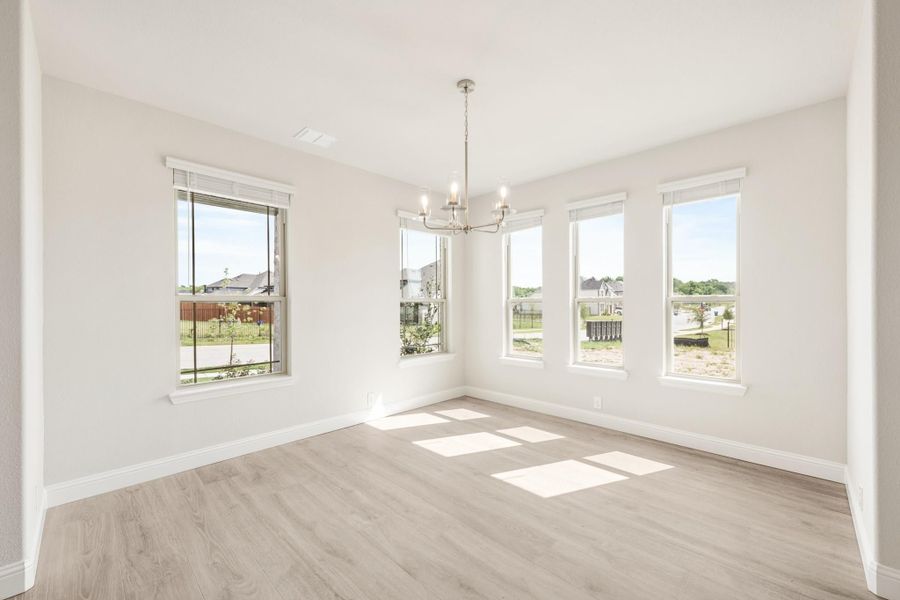 Empty dining room with light wood floors, chandelier, and four large windows