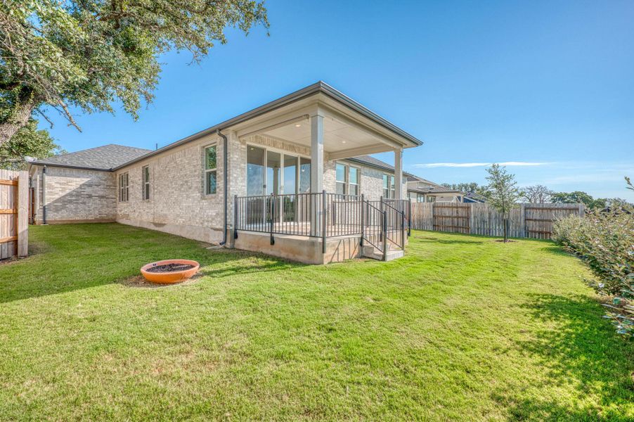 A spacious green lawn borders the brick exterior and covered back patio of this home.