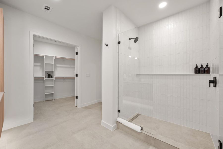 The primary bath in the Shady Grove palette features warm cabinetry, black hardware, quartz countertops, and a glass enclosed shower for a clean, modern look.