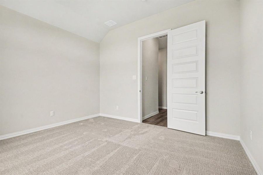 Spacious room featuring light-toned carpeting, neutral wall paint, white baseboards, and a vaulted ceiling Spacious room featuring light-toned carpeting, neutral wall paint, white baseboards, and a vaulted ceiling