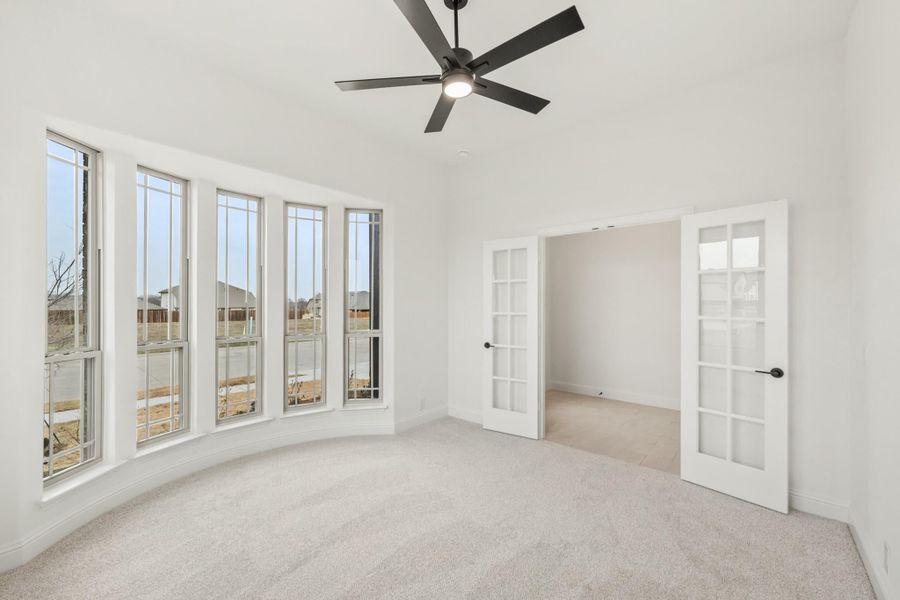 Empty bedroom with curved bay windows, ceiling fan, carpet, and French doors leading to adjoining room