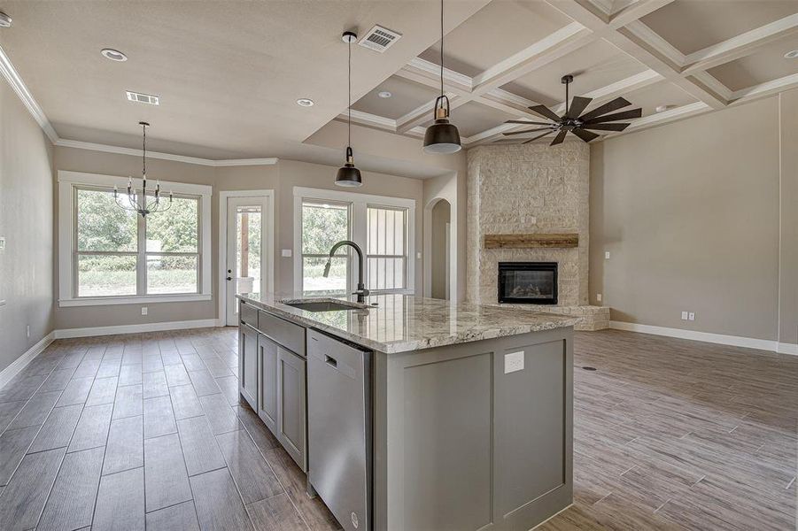 Kitchen with sink, light stone counters, stainless steel dishwasher, coffered ceiling, and a kitchen island with sink