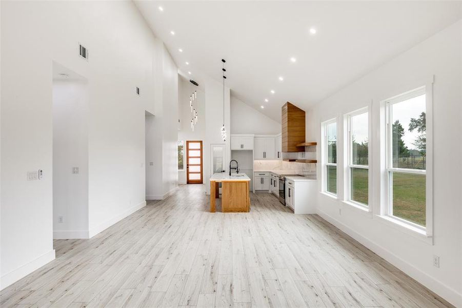 Kitchen with open shelves, white cabinets, open floor plan, high vaulted ceiling, and light wood-style floors Kitchen with open shelves, white cabinets, open floor plan, high vaulted ceiling, and light wood-style floors