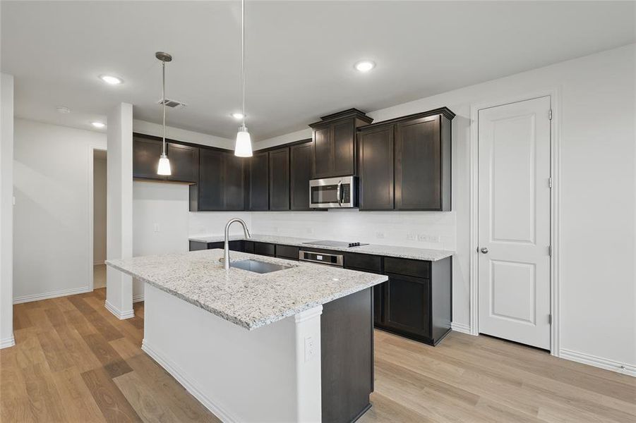 Kitchen with stainless steel microwave, a sink, light wood finished floors, light stone counters, and baseboards Kitchen with stainless steel microwave, a sink, light wood finished floors, light stone counters, and baseboards