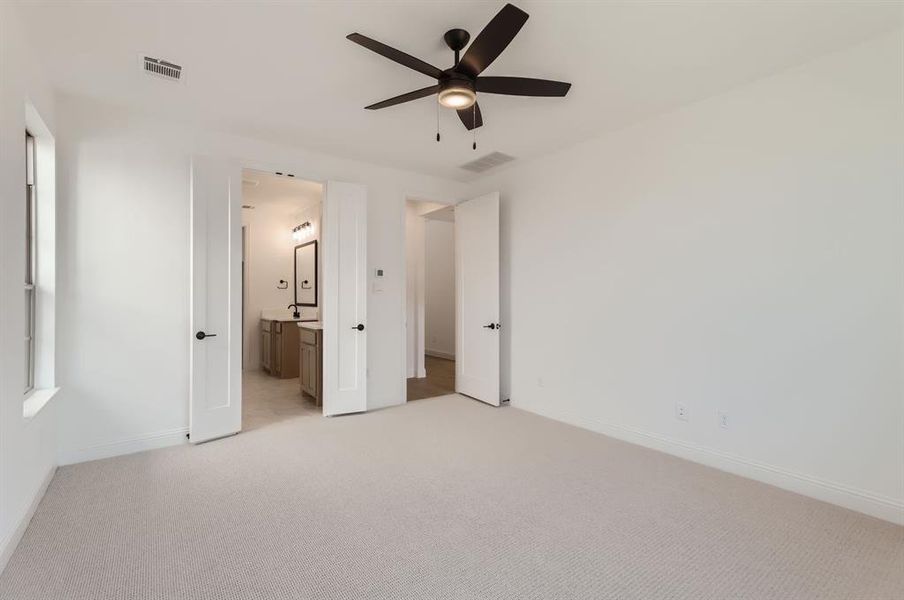 Unfurnished bedroom with connected bathroom, light colored carpet, and ceiling fan