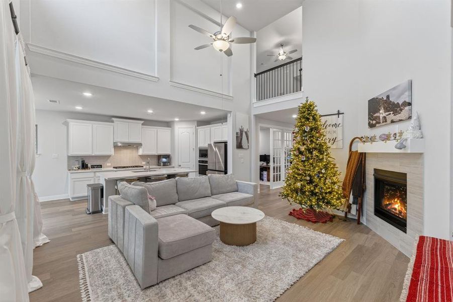 Living room with light wood finished floors, a fireplace, a ceiling fan, a high ceiling, and recessed lighting Living room with light wood finished floors, a fireplace, a ceiling fan, a high ceiling, and recessed lighting