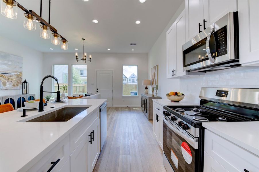 Full kitchen showing white shaker cabinets with matte black hardware, quartz countertops, subway tile backsplash, stainless appliances including range, microwave, and dishwasher, farmhouse sink, and Edison pendant rail lighting.