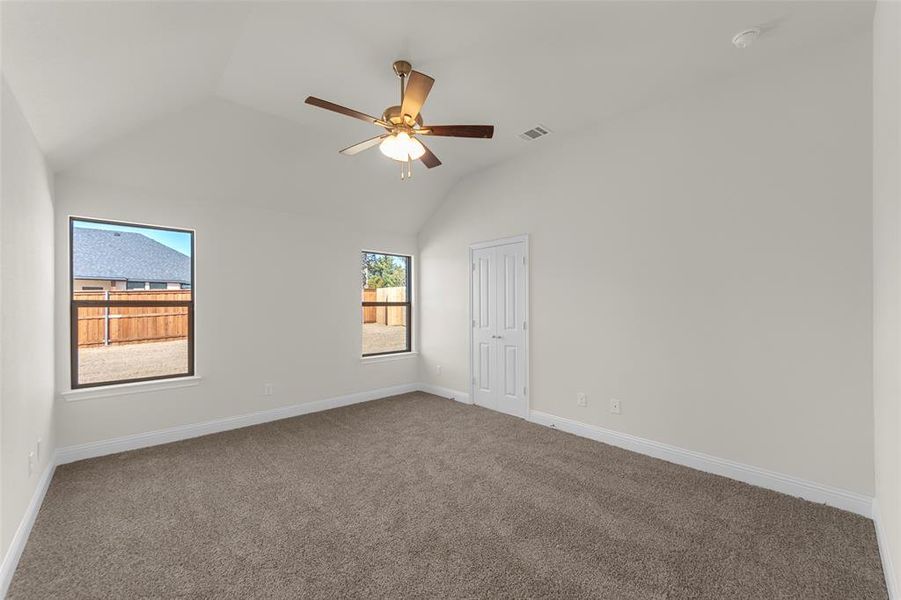 Carpeted empty room featuring vaulted ceiling and a ceiling fan