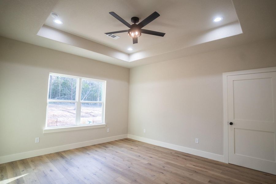 Unfurnished room with a ceiling fan, a tray ceiling, wood finished floors, and baseboards