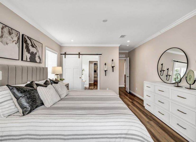 Bedroom featuring a barn door, dark wood finished floors, ornamental molding, and recessed lighting