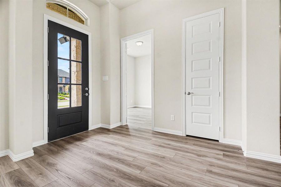 Entryway featuring a black multi-pane glass door with an arched transom window, wood-finish flooring, and crisp white baseboards and trim Entryway featuring a black multi-pane glass door with an arched transom window, wood-finish flooring, and crisp white baseboards and trim