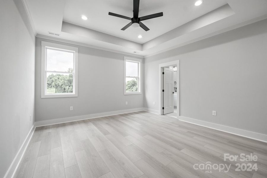 Primary bedroom with large ceiling fan and tray ceilings