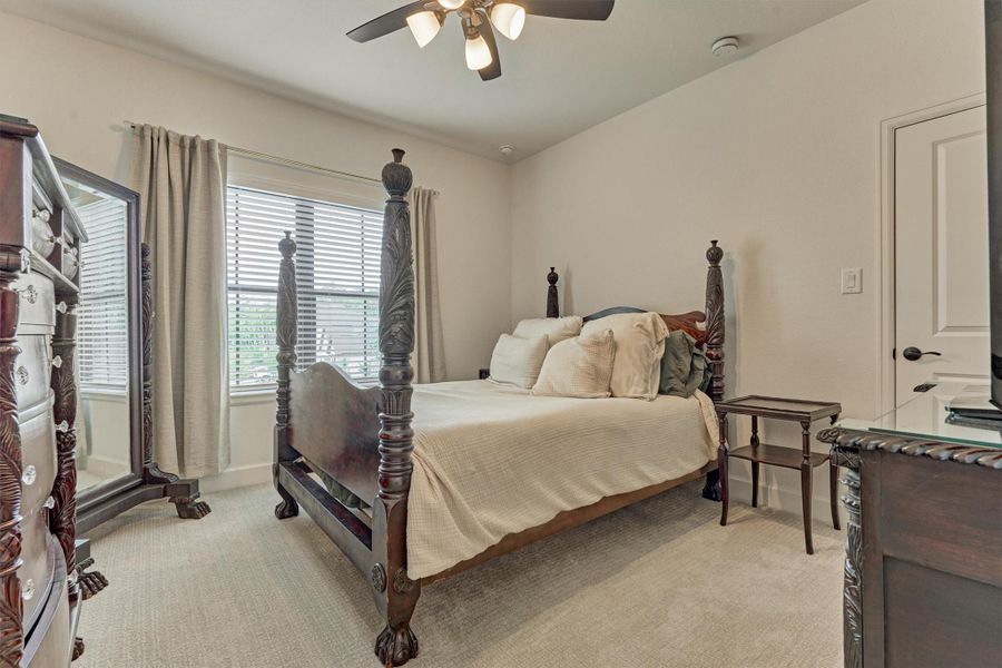 This inviting secondary bedroom (3) offers a serene retreat with its elegant four-poster bed, plush carpeting, and ample natural light streaming through the window, creating a cozy and stylish space for relaxation.