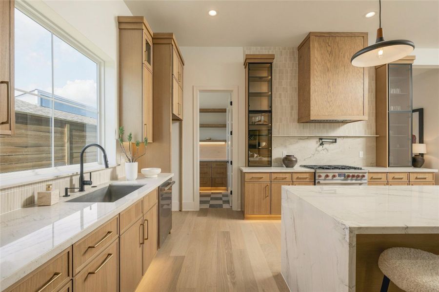 A closer view reveals the kitchen’s layered craftsmanship, where custom white oak details, glass-front cabinetry, and integrated LED lighting bring warmth and dimension to the space.