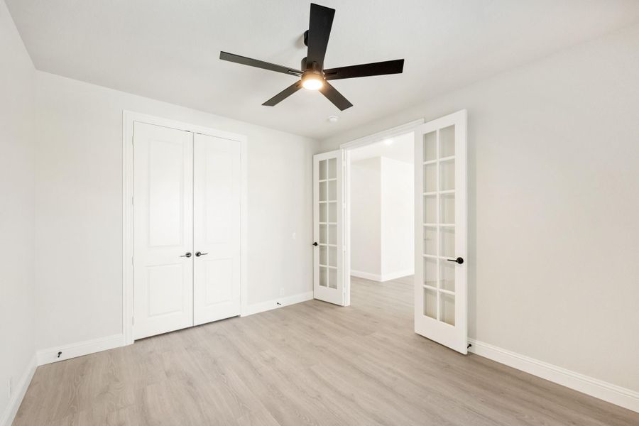 Empty bedroom with light wood floors, ceiling fan, double closet, and French doors