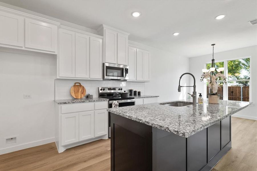 Kitchen with appliances with stainless steel finishes, an island with sink, white cabinets, light stone countertops, and sink