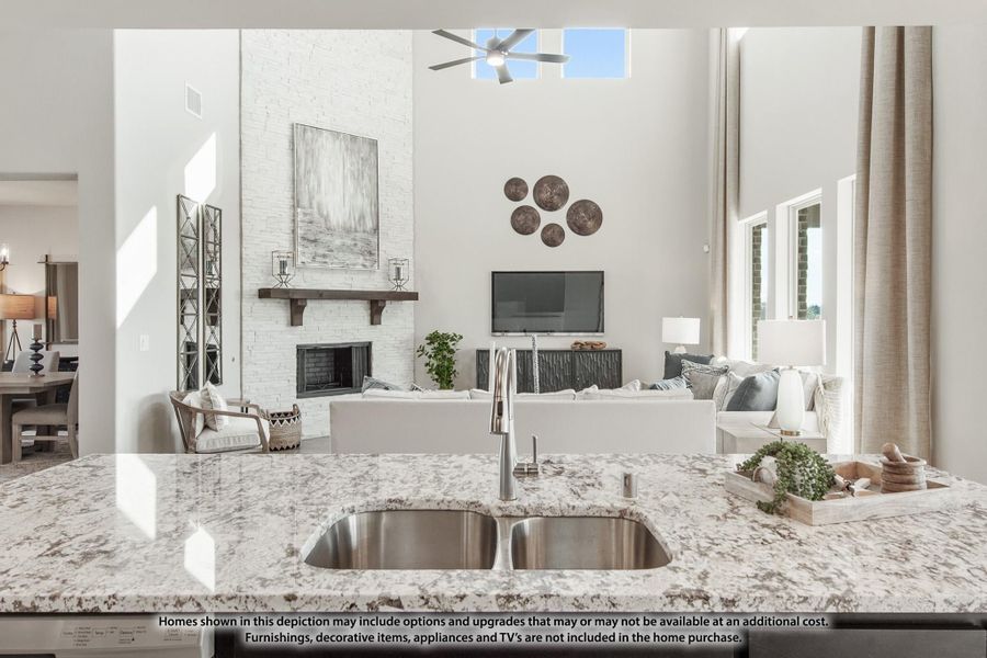 Open-concept living area with granite kitchen island, white brick fireplace, and two-story ceiling with ceiling fan Open-concept living area with granite kitchen island, white brick fireplace, and two-story ceiling with ceiling fan