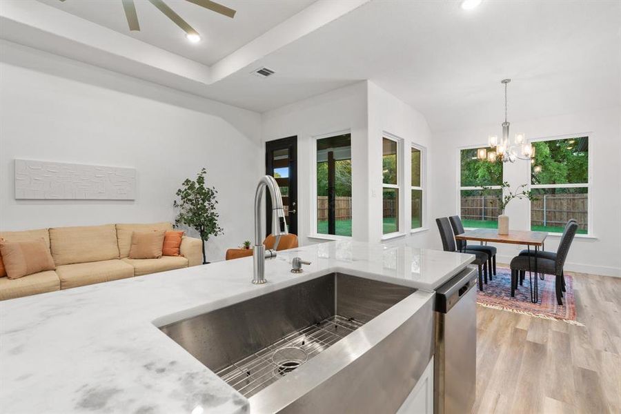 Kitchen with light stone counters, hanging light fixtures, sink, light hardwood / wood-style flooring, and dishwasher