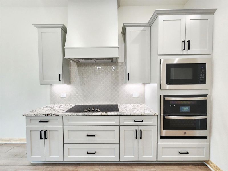 Kitchen featuring light-toned cabinetry with black hardware, a built-in cooktop, and granite-style countertops