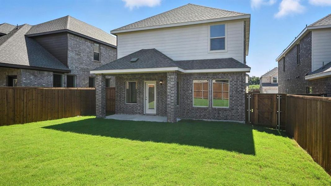 Rear view of property featuring brick siding, a patio, roof with shingles, and a gate