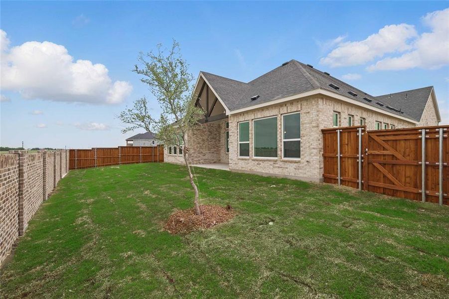 Rear view of house with roof with shingles, a gate, brick siding, a fenced backyard, and a yard