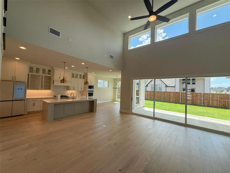 Unfurnished living room with plenty of natural light, a towering ceiling, light wood-style flooring, recessed lighting, and a ceiling fan Unfurnished living room with plenty of natural light, a towering ceiling, light wood-style flooring, recessed lighting, and a ceiling fan