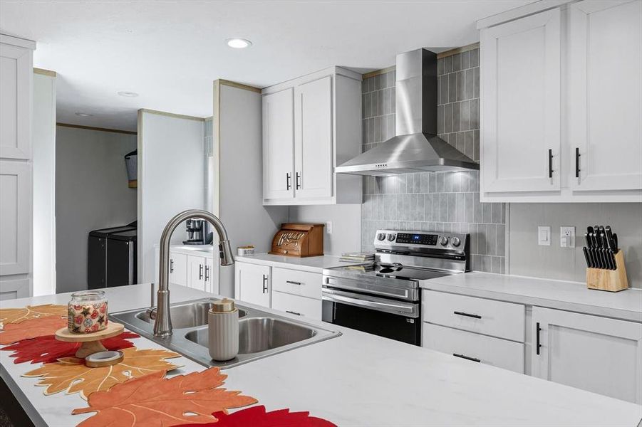 Kitchen featuring light countertops, stainless steel electric stove, wall chimney exhaust hood, white cabinetry, and recessed lighting Kitchen featuring light countertops, stainless steel electric stove, wall chimney exhaust hood, white cabinetry, and recessed lighting