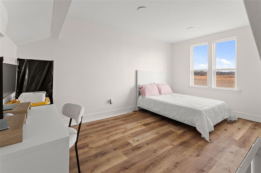 Bright room featuring dual windows with white trim, wood-finish flooring, a white headboard, and a white baseboard Bright room featuring dual windows with white trim, wood-finish flooring, a white headboard, and a white baseboard