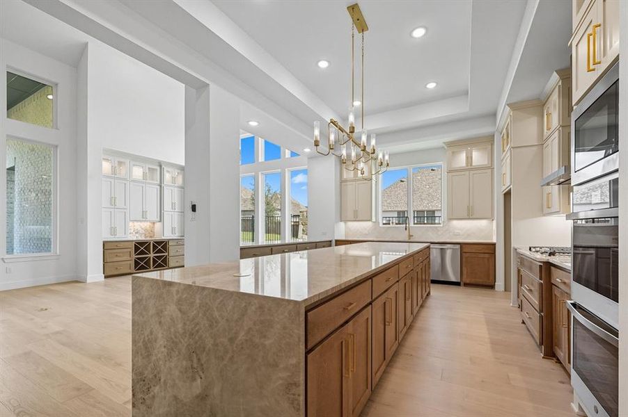 Kitchen with brown cabinetry, glass insert cabinets, decorative backsplash, light stone countertops, and recessed lighting Kitchen with brown cabinetry, glass insert cabinets, decorative backsplash, light stone countertops, and recessed lighting