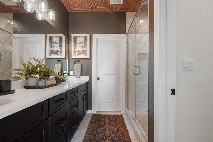 Bathroom featuring a double vanity with white countertops, dark wood-finish cabinetry, and a glass-enclosed shower with tile surround