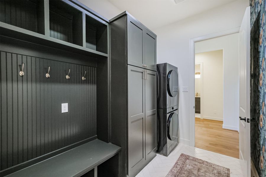 Mudroom/laundry with dark custom cabinetry, bench seating, hooks, and stacked washer/dryer.