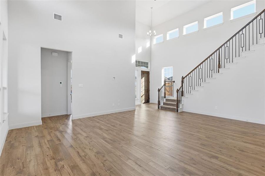 Unfurnished living room with stairway, light wood finished floors, a chandelier, and a towering ceiling