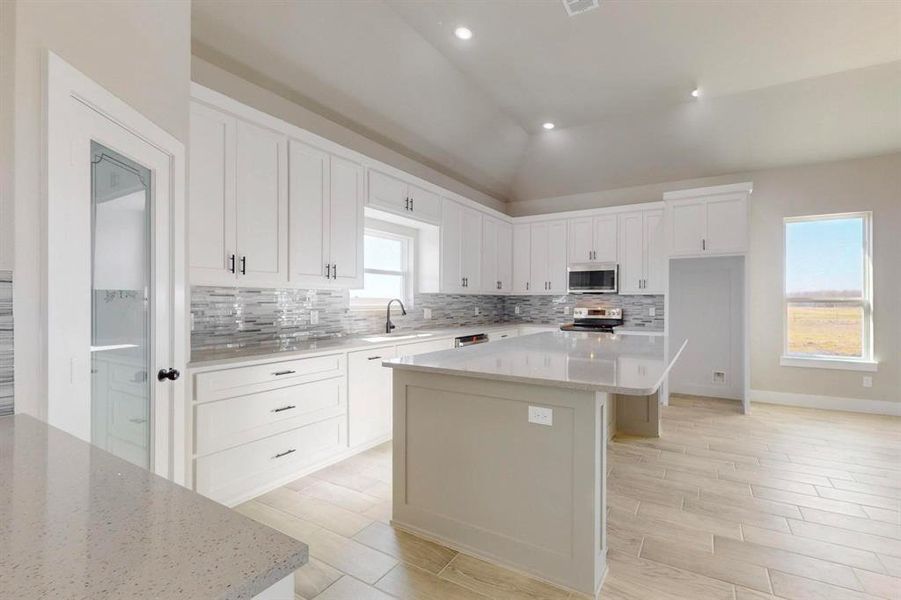 Kitchen with backsplash, a center island, appliances with stainless steel finishes, white cabinets, and a sink