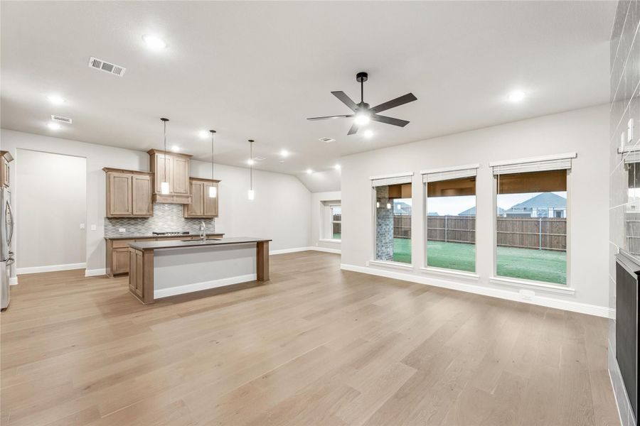 Open-concept living area and kitchen with wood cabinets, center island, hardwood floors, and ceiling fan
