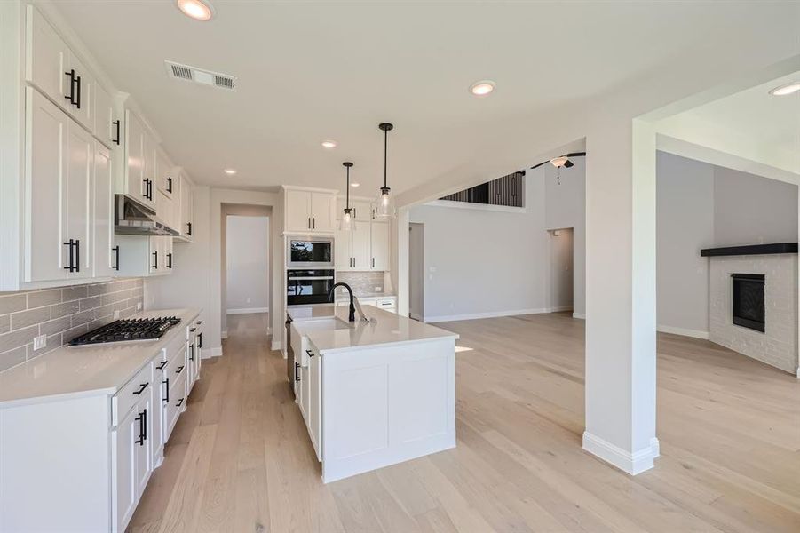 Kitchen with pendant lighting, an island with sink, backsplash, white cabinetry, and stainless steel appliances