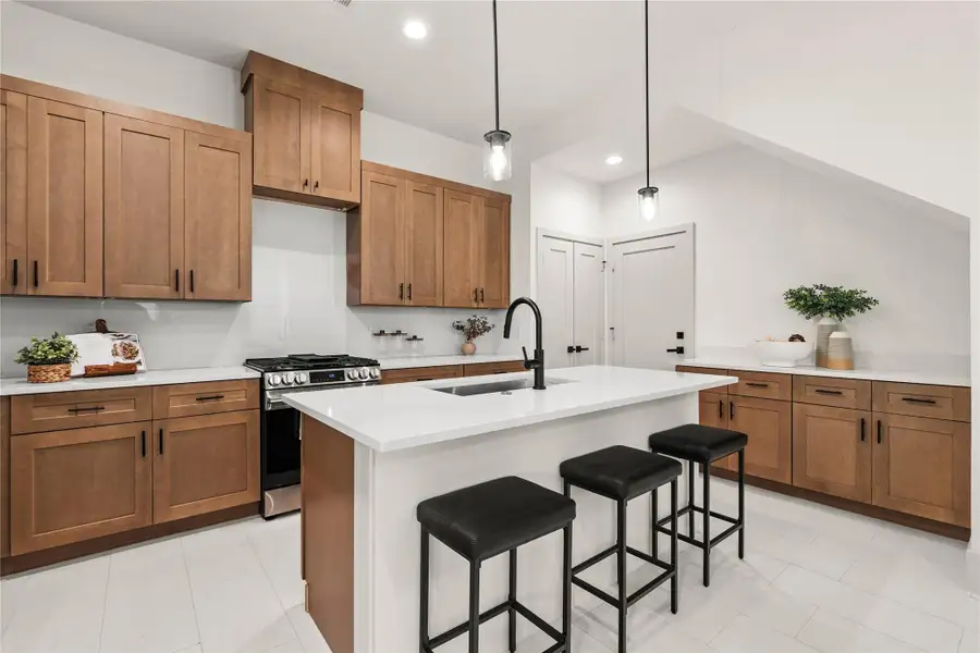Kitchen with warm shaker cabinetry, gas range, quartz island, and pendant lights Kitchen with warm shaker cabinetry, gas range, quartz island, and pendant lights