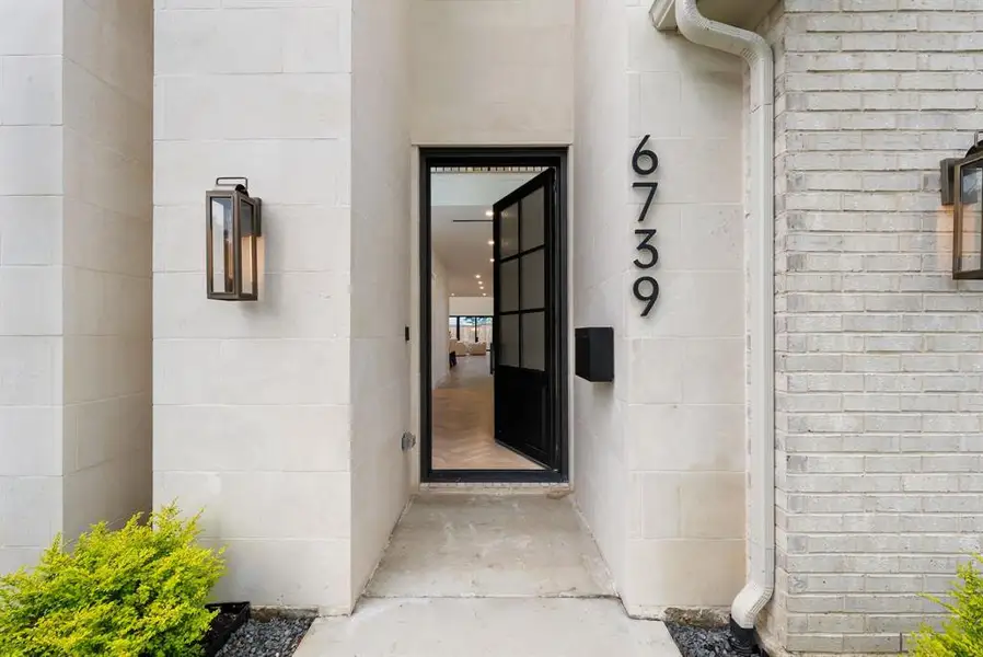 The property features a concrete walkway leading to an entryway with a dark-framed glass door, flanked by light-colored stonework and a brick facade