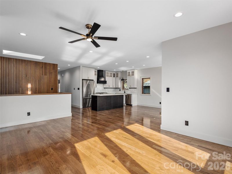 Open-concept main living area with oak hardwood floors, flowing from the living room to the dining area, kitchen, hallway with elevator, and stairwell.