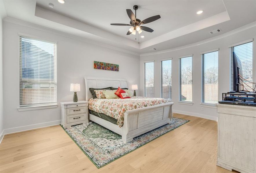 Bedroom with light hardwood / wood-style floors, a raised ceiling, ceiling fan, and crown molding