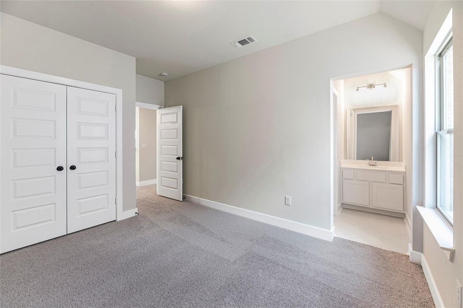 Unfurnished bedroom featuring light carpet, ensuite bath, and a closet