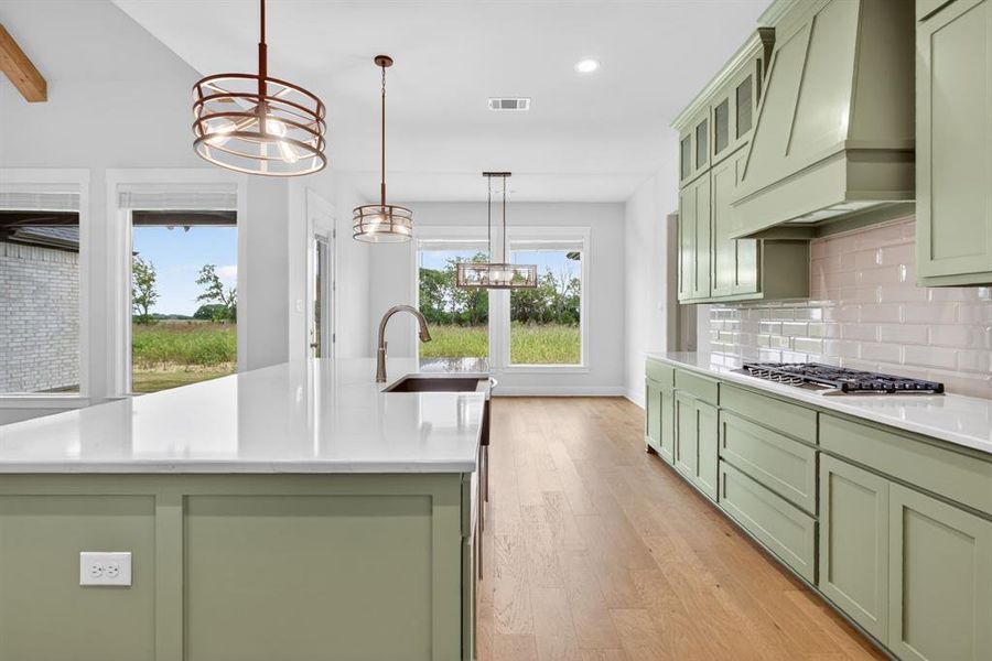 Gourmet kitchen featuring sage green shaker cabinetry, quartz countertops, a gas range with a custom range hood, and a large island with an undermount sink Gourmet kitchen featuring sage green shaker cabinetry, quartz countertops, a gas range with a custom range hood, and a large island with an undermount sink