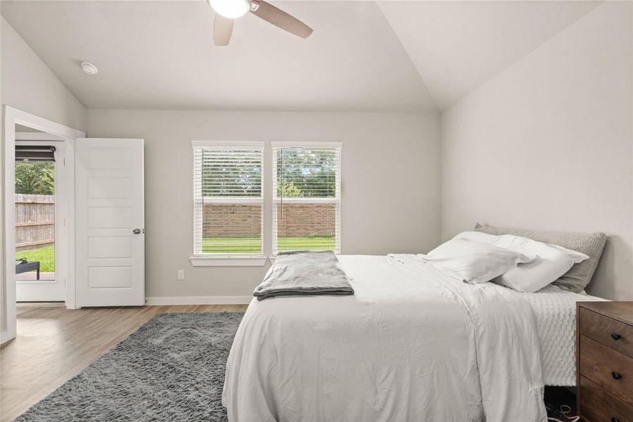 his light-filled bedroom features soaring vaulted ceilings, expansive windows, and stylish wood-look flooring that enhances the airy, modern feel. The generous layout easily accommodates large furniture while maintaining a relaxing atmosphere.